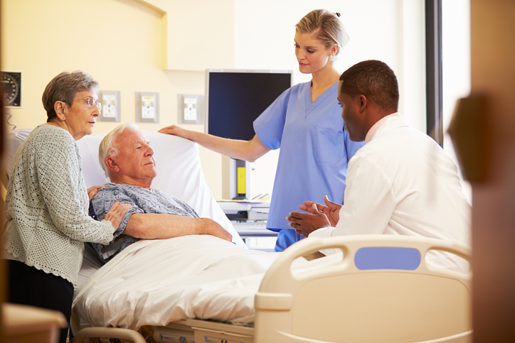 Medical Team Meeting With Senior Couple In Brightly Lit Hospital Room